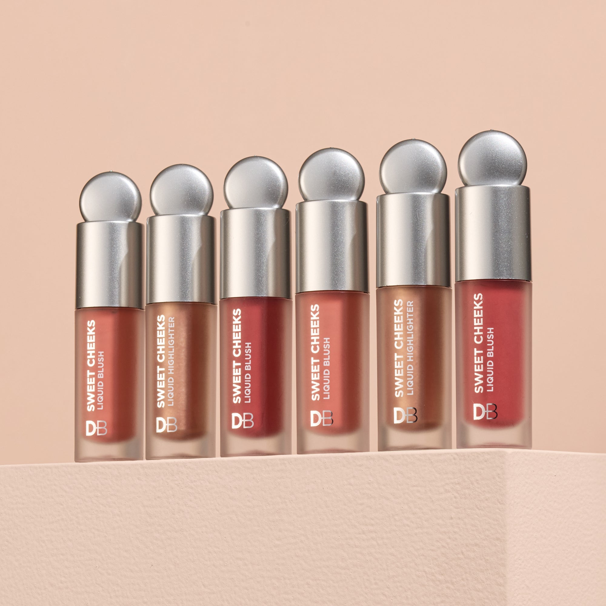 Set of 'Sweet Cheeks' liquid blushes with silver caps on a beige background