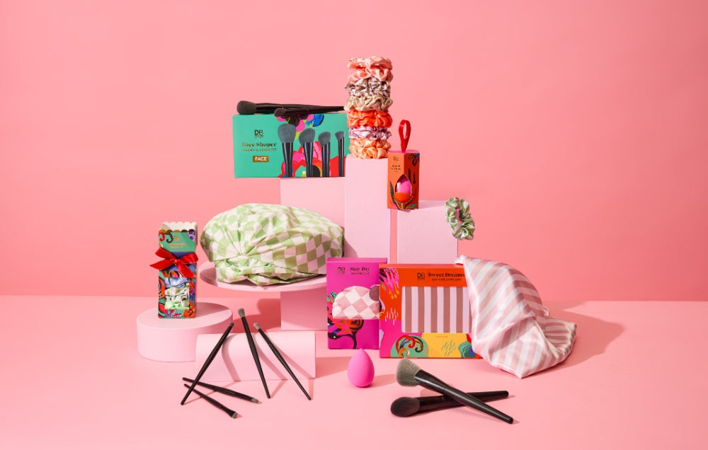 A vibrant display of luxury jewellery boxes, hair accessories, and makeup brushes arranged on a pink backdrop, exuding elegance and style.