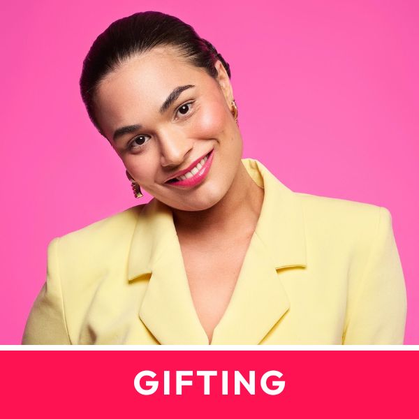 Smiling person in a yellow blazer with elegant earrings against a pink background. Text reads "GIFTING" below. Luxurious jewellery concept.