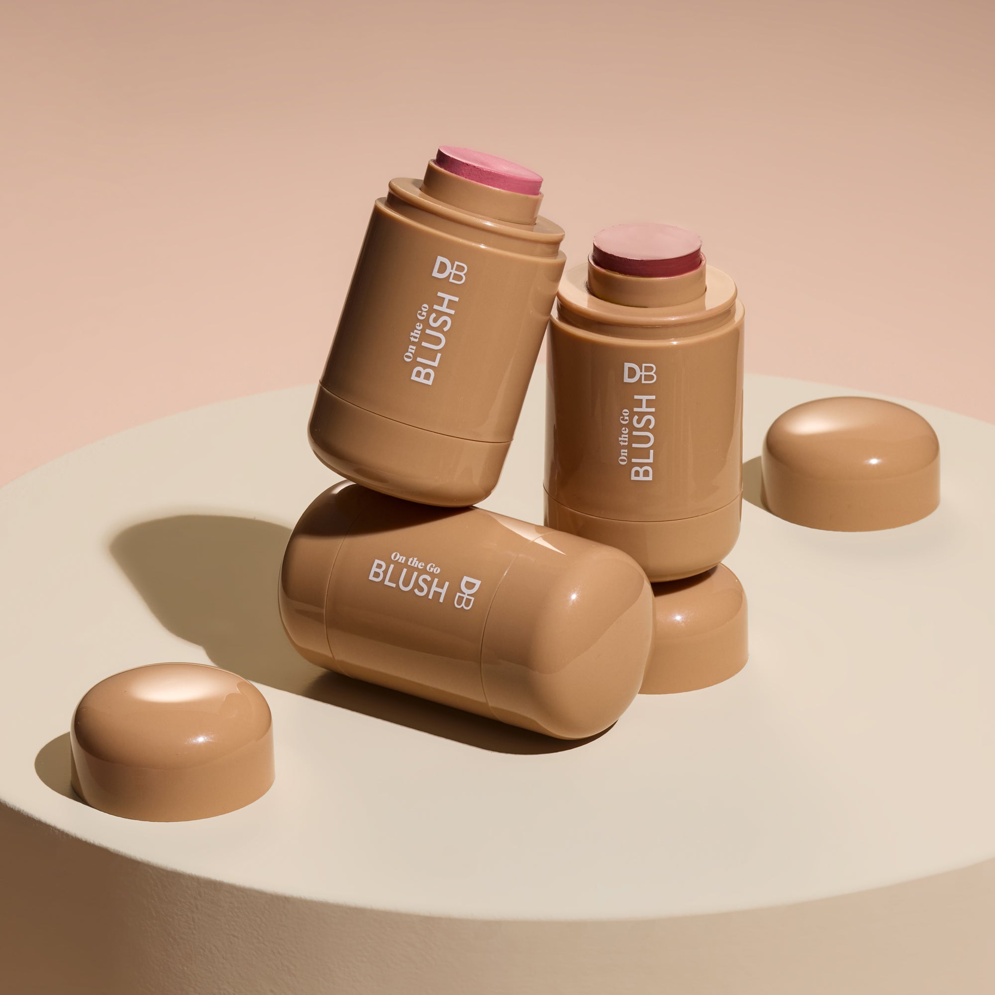 Three blush sticks with pink caps on a beige surface