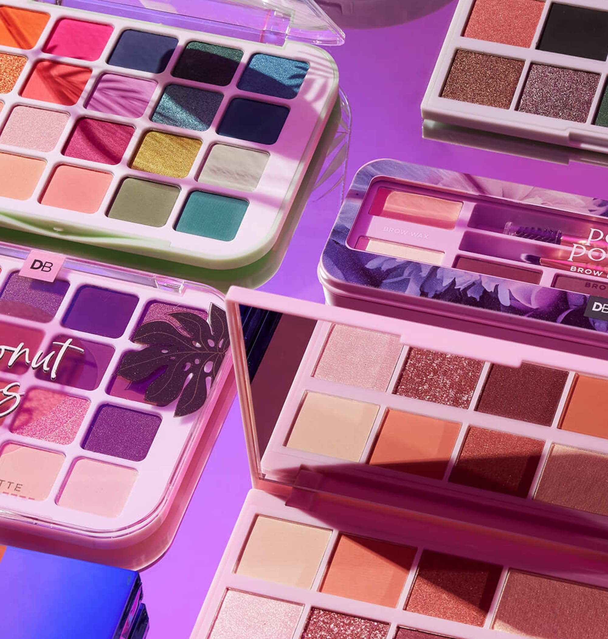 Vibrant eyeshadow palettes with diverse colours, set on a reflective purple surface, showcasing exquisite makeup shades.