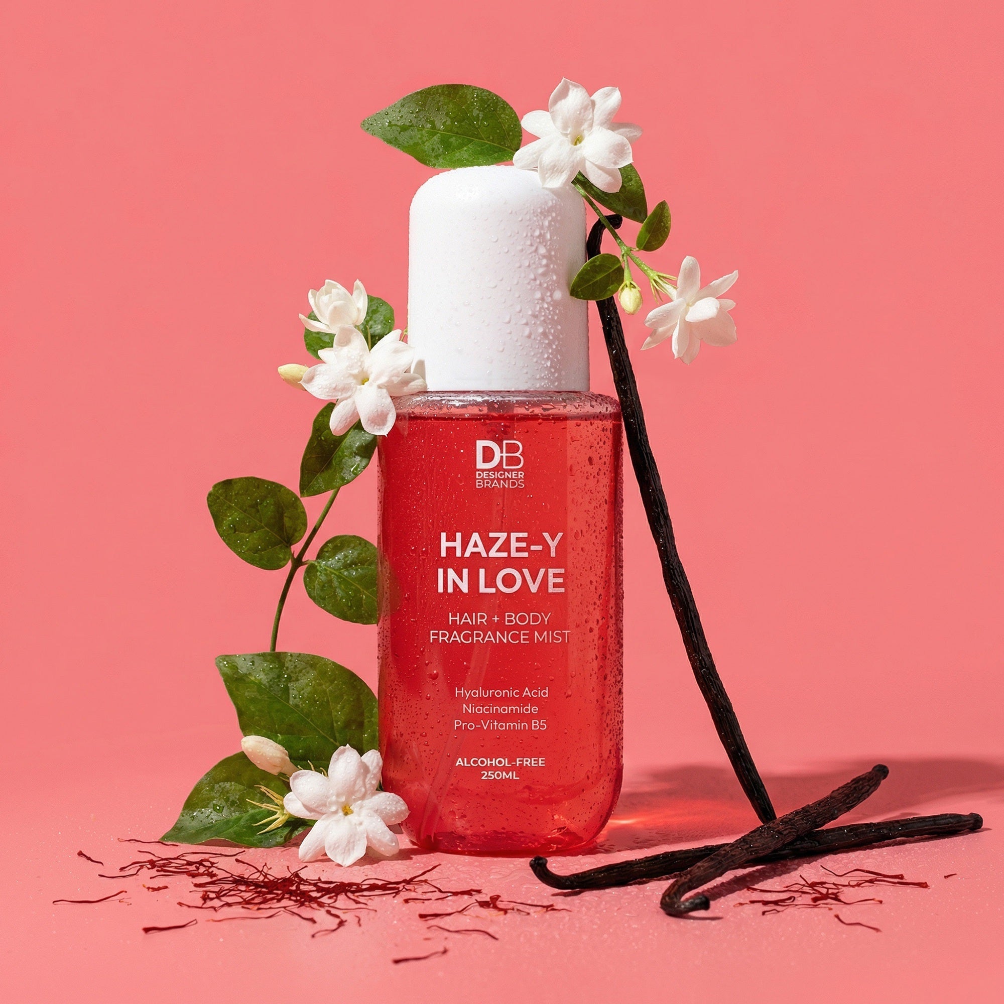 Hair and body mist bottle with flowers and vanilla beans on a pink background