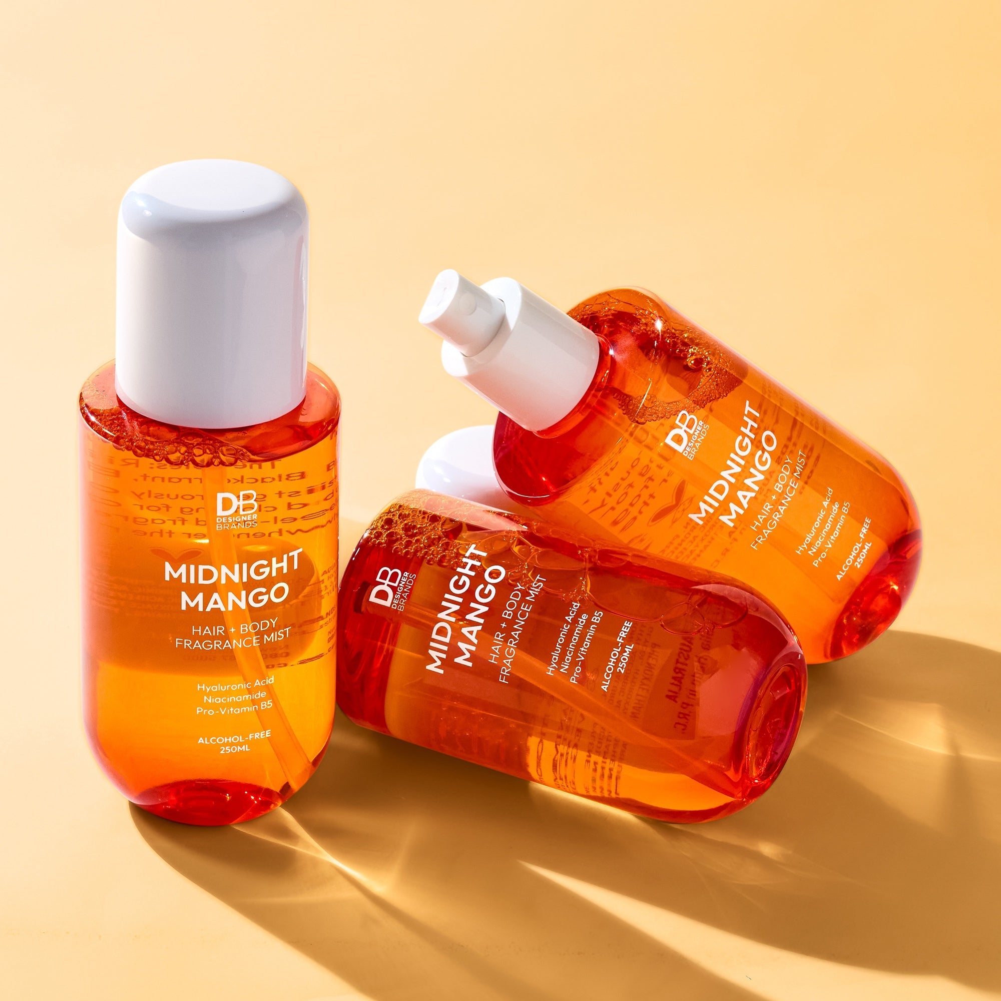 Three bottles of 'Midnight Mango' fragrance mist on a beige background